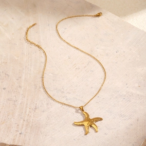Minimalist gold starfish pendant necklace on stone background for beach vacation