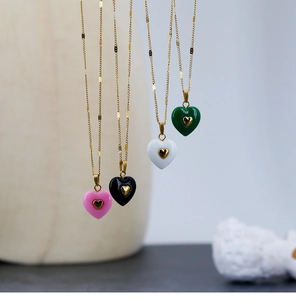 Close-up of heart pendant necklaces in pink, black, white, and green with gold chains