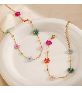 Close-up of gold chain necklace with colorful bead flowers on white ceramic tray