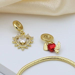 Elegant gold heart charms with red enamel wings on snake chain over silk background