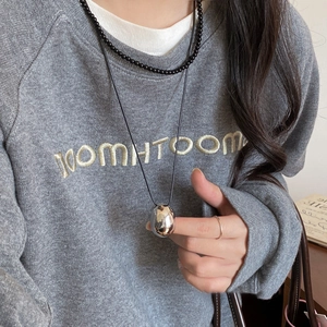 Detail of silver waterdrop pendant with black cord necklace on gray sweatshirt