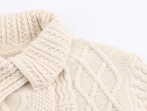 Nahaufnahme der Zopfmuster-Textur und des beigefarbenen Strickstoffs an der Strickjacke