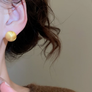 Close-up of a minimalist golden brushed metal spherical earring worn by a model