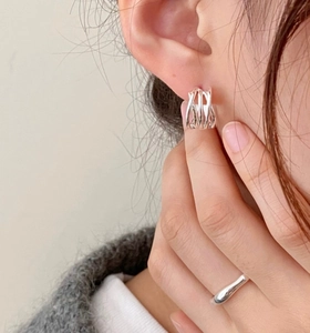 Macro shot of a woman wearing silver braided hoop earrings and a minimalist ring