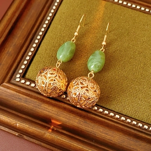 Detail of vintage gold hollow ball earrings with green oval jade beads on dark green fabric
