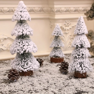 Three miniature green Christmas trees with fake snow and pine cones on a wooden base