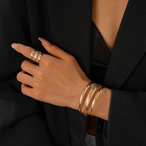 Detail of layered gold bangles and ring set worn with a black blazer for a premium look