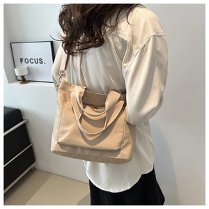 Detalle de un bolso bandolera beige grande de nailon con bolsillo frontal y acabado crema
