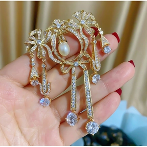 Détail macro d'une broche nœud vintage dorée avec glands en zircon et une perle goutte