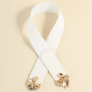 Close-up of white elastic waist belt with gold metal bow buckle on beige background