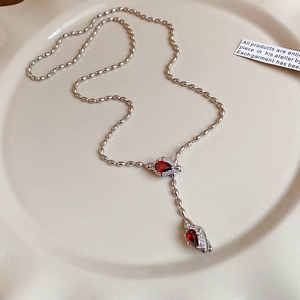 Detailed macro view of silver Y-shaped necklace with red zircon teardrop pendants on a plate