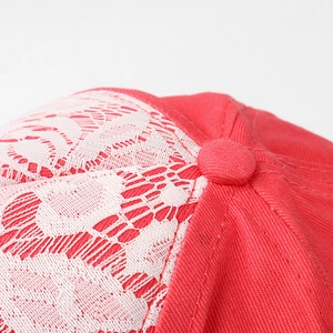 Détail de casquette en sergé rouge avec broderie en dentelle blanche et bouton en tissu
