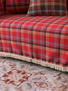 Detail of red festive plaid sofa cover with cream tassels and matching throw pillow