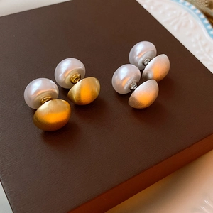 Detailed close-up of double-sided gold and silver pearl earrings on a brown textured box