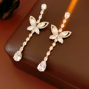Macro detail of gold butterfly drop earrings with clear zircon on a leather surface