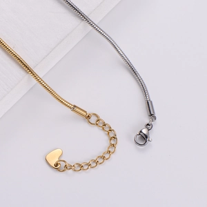 Close-up of gold and silver snake chain bracelets with lobster clasp and heart charm