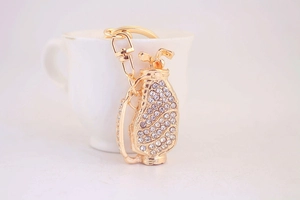 Detailed close-up of golden golf bag keychain with sparkling rhinestones on white desk