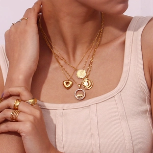 Detailed close-up of layered 18K gold-plated evil eye and heart necklaces on a model