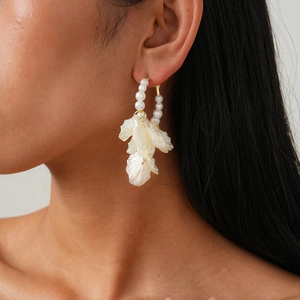 Détail de boucles d'oreilles pendantes avec perles blanches et pétales en métal doré