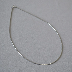 Dettaglio di una collana girocollo a spirale color argento su sfondo grigio testurizzato