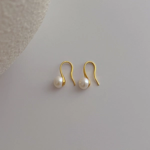Detail shot of golden hook earrings featuring white freshwater pearls on a soft grey background
