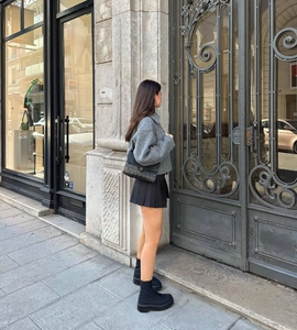 Detail shot of a grey cropped wool jacket paired with a black pleated skirt and tall boots