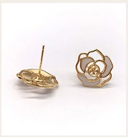 Macro shot of gold-plated camellia earrings with white enamel and 925 silver posts