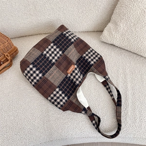 Dettaglio della borsa tote in tweed con motivo a scacchi marroni e etichetta su divano