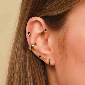 Close-up of gold ear cuff and cartilage studs with black stones on female model