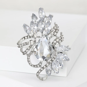 Detailed macro view of a silver crystal brooch with pear-cut rhinestone on a white pedestal