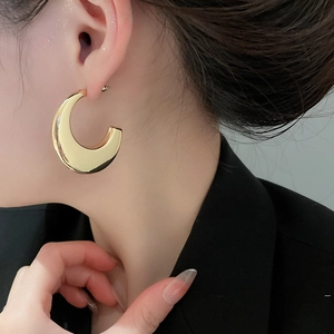 Close-up of a large polished gold C-shaped hoop earring worn by a female model