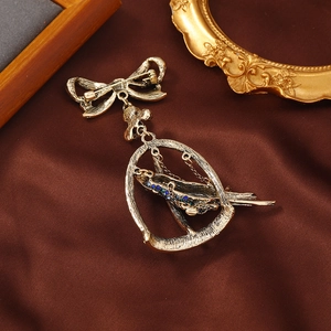Vintage gold bow brooch with rhinestone parrot in a birdcage over silk background