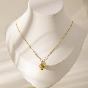Detail of vintage gold necklace with green gemstone pendant on a white neck mannequin