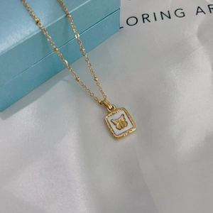 Detail of a gold square butterfly pendant on a beaded chain over white silk fabric
