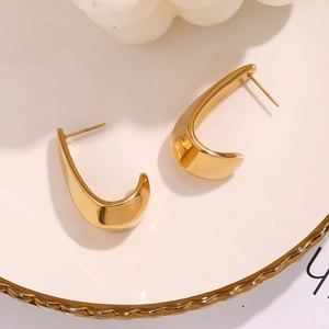 Macro detail of gold-plated hollow geometric hook earrings on a white ceramic tray