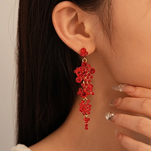 Detail of red rhinestone tassel earrings with golden metal base worn by a female model