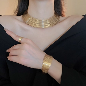 Detail view of layered gold metal necklace and wide cuff bracelet on model with black top