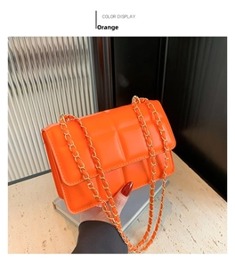Detail of orange quilted crossbody bag featuring plush checkered texture and gold chain strap