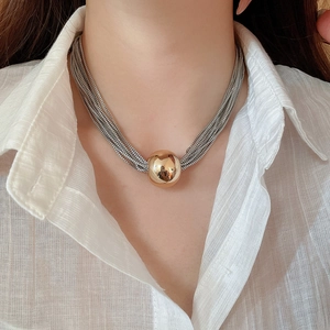 Detail of layered silver chain necklace featuring a bold golden metallic sphere pendant