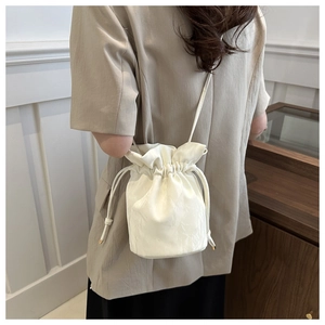 Detail of a white satin drawstring bucket bag worn with a beige blazer for chic styling
