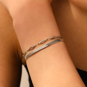 Détail de bracelets superposés avec chaîne géométrique et chaîne serpent au poignet