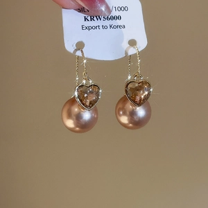 Detail of drop earring with golden chain, heart-shaped brown gem and champagne pearl