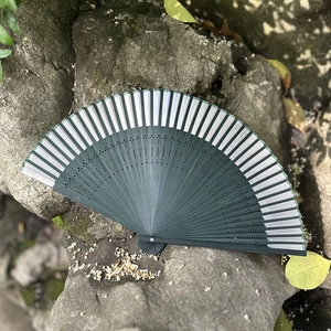 Traditional green bamboo folding fan with hollow carving on mossy rock surface