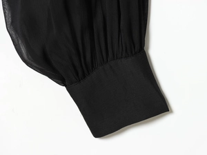 Primer plano del puño de una blusa de gasa negra con detalles plisados y costuras