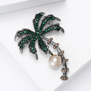 Detail of palm tree brooch with green crystals and white pearl on metal finish