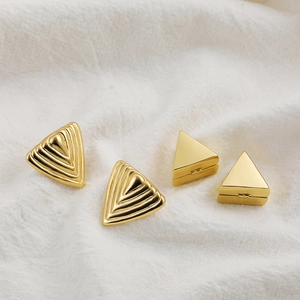 Macro shot of 18K gold plated hollow geometric triangle earrings on white linen fabric