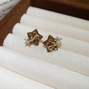 Detail of 18k gold star earrings with brown enamel, cat motif and zircon on beige velvet