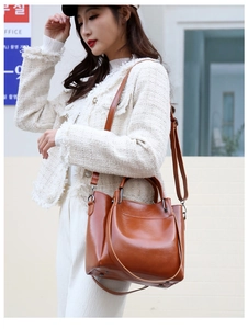 Close-up of brown leather handbag with metallic hardware and adjustable strap on a model