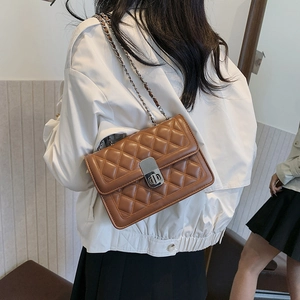 Detail of dark brown quilted leather crossbody bag with chain strap and metal clasp on model