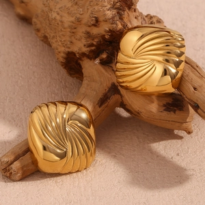 Macro detail of square gold earrings with radial texture on a natural wooden branch
